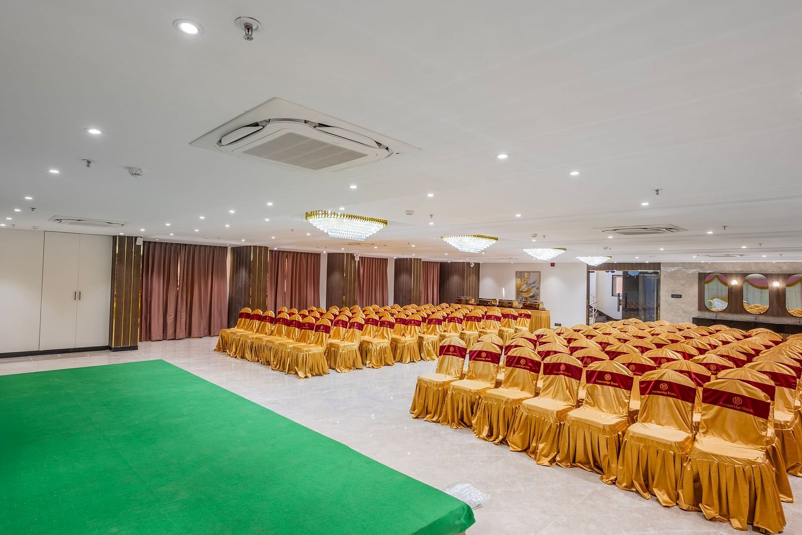 Lemonridge Hotels, KPHB | Banquet hall with an aisle, set up with rows of chairs for a formal event. Clean and maintained space.